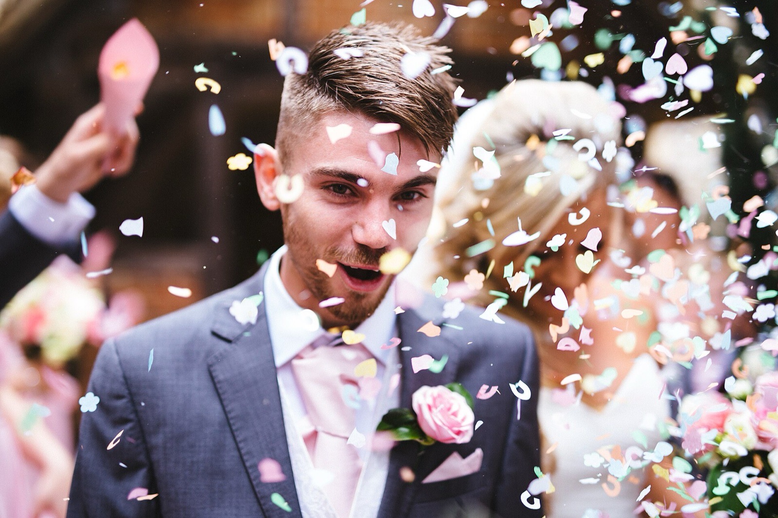 Groom laughing as colourful confetti falls around the couple