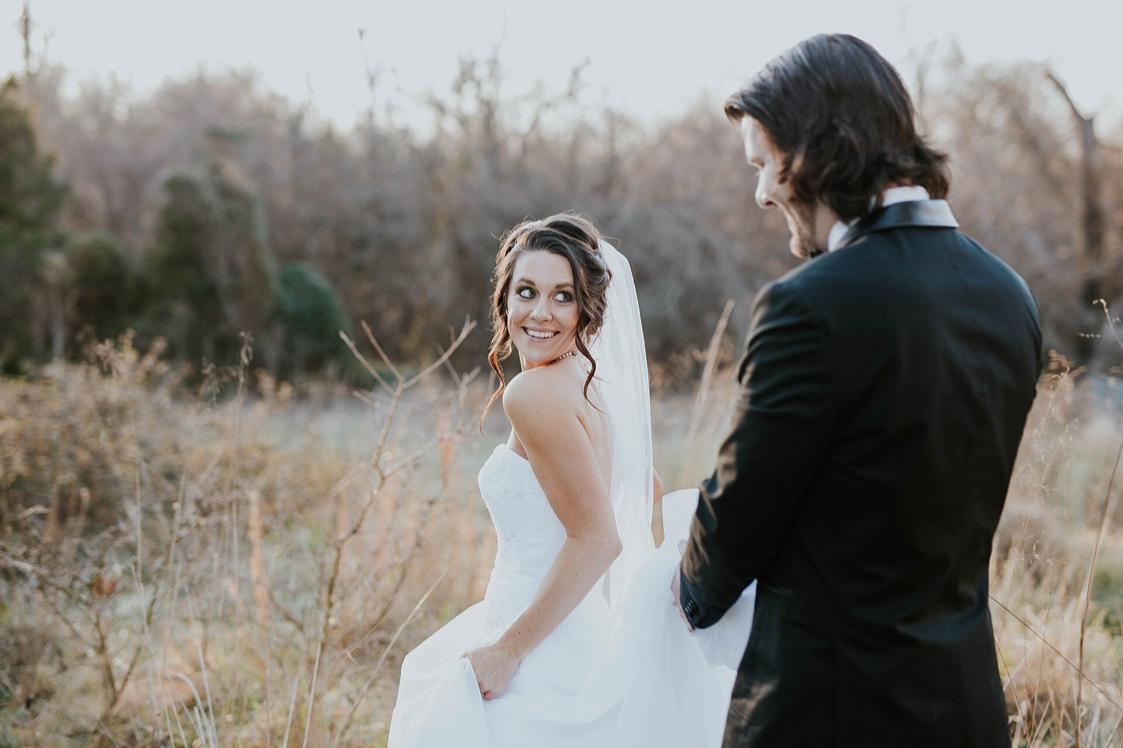 Bride smiling back at the groom outdoors after their wedding