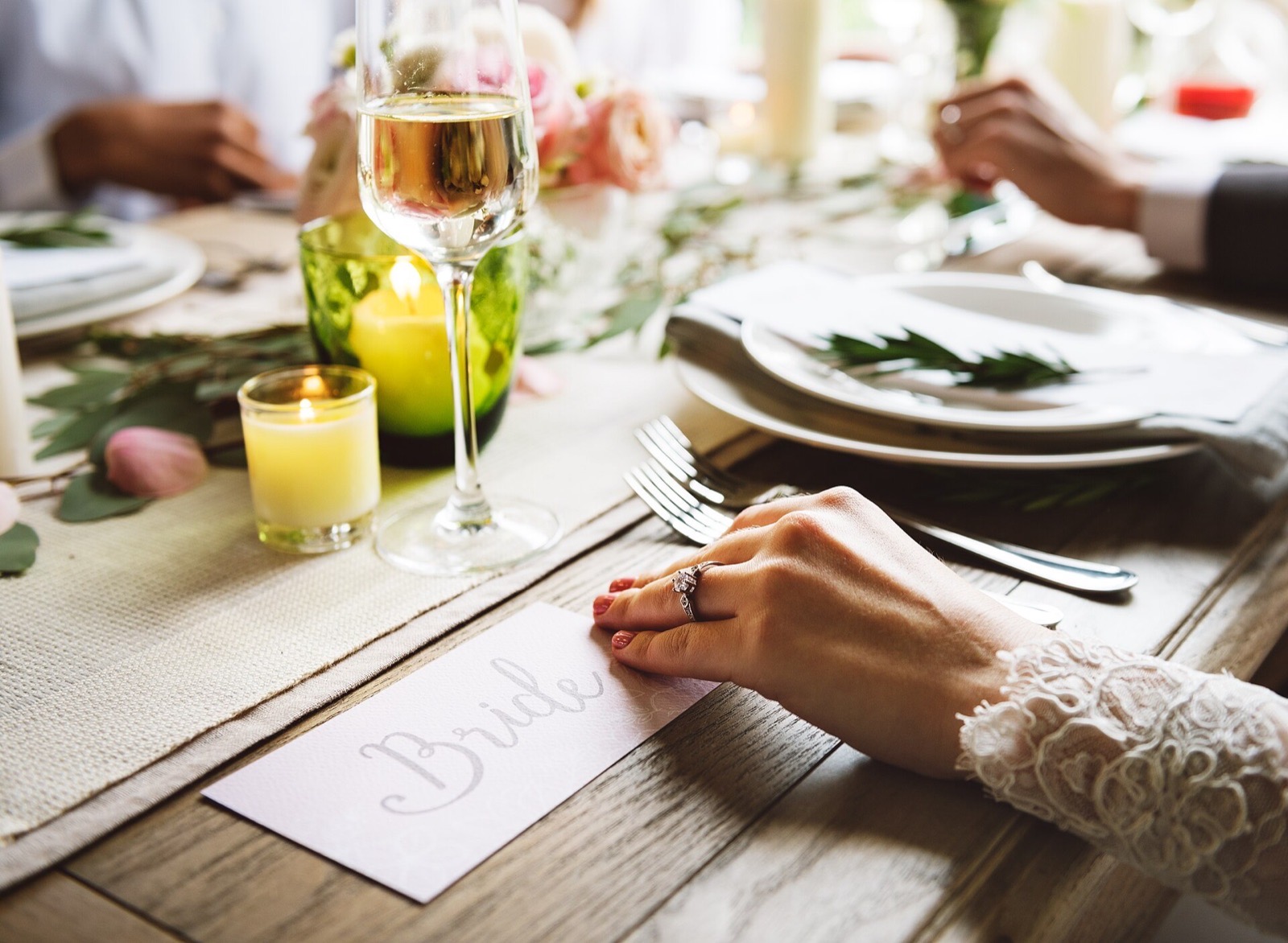 Bride’s hand beside a wedding place setting, candles and champagne